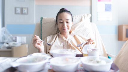 Obraz na płótnie Canvas Asian woman lying on the hospital bed for admitting and she is ating breakfast. Hospitalization concept.