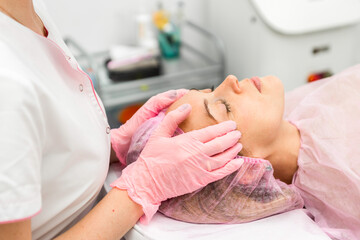Fototapeta na wymiar Beautician does facial care procedure for young woman in beauty salon