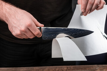 Man testing sharpness of knife by cutting a thin sheet of paper