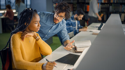 University Library: Gifted Black Girl uses Laptop, Smart Classmate Explains and Helps Her with Class Assignment. Happy Diverse Students Talking, Learning, Studying Together for Exams