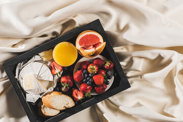 top view of french breakfast with grapefruit, Camembert, orange juice, berries and baguette on tray on white tablecloth