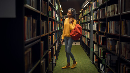 University Library: Portrait of Gifted Beautiful Black Girl Stands Between Rows of Bookshelves Searching for the Right Book for Class Assignment. Focused Smart Student Learning, Studying for Exams