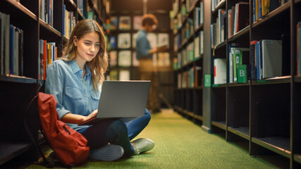 University Library: Gifted Beautiful Caucasian Girl Sitting On Floor, Uses Laptop, Writes Notes for Paper, Essay, Study for Class Assignment. Diverse Group of Students Learning, Studying for Exams.