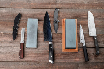 Assortment of knives and whetstones on rustic wooden background, top view