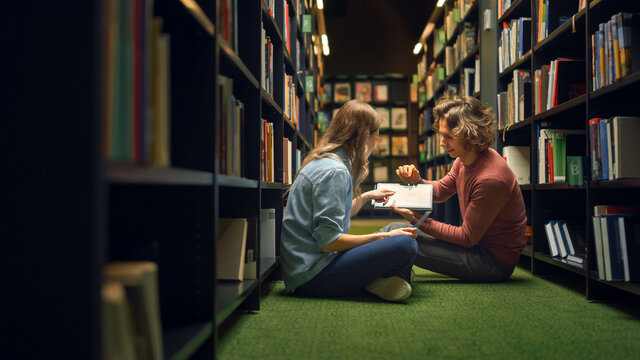 University Library: Smart Girl Sitting and Talented Boy Sitting Cross-Legged On the Floor, Talk, Use Digital Tablet and Discuss Paper, Study and Prepare for Exams Together. Authentic Students