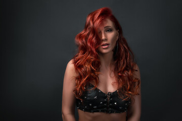 Fototapeta premium sexy girl posing against black background with copy space. beautiful woman wearing leather top bra with sparkling stars. red colored hair and professional make up