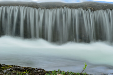 milky white river flood torrent over concrete barrier in summer, long exposure
