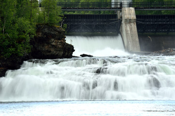 Obraz premium massive white waterfall down rocks as water power plant opens concrete barrier