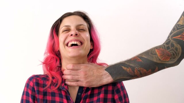 Male hand in tattoos strangles woman by the throat. Woman uncontrollably nervously laughs at the criminal. Self-isolation domestic violence. Prohibition of freedom of speech.