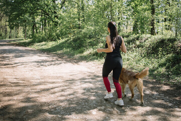 Back view of girl running along the road in the countryside with dog. Back of girl wearing sportswear jogging in forest with her dog.