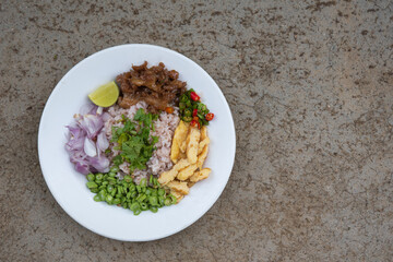 Caramelized pork and rice mixed with shrimp paste in white plate on concrete background.
