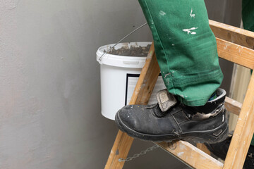 A professional construction worker stands on a wooden ladder in boots and work clothes.