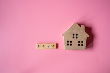 The words "save" made with wooden letters and small wooden toy house on pink background.