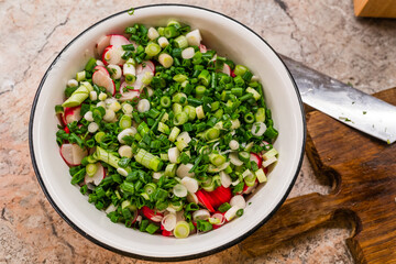 Salad with radish and onion in white metal plate on the table near wooden cutboard and knife. Selective focus
