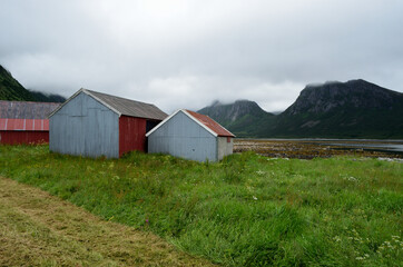 Fototapeta na wymiar beautiful old fishing boat houses next to summer fjord with mountain background
