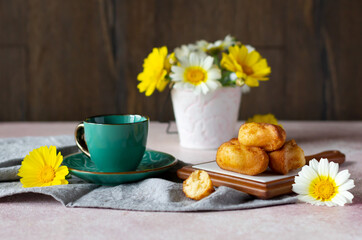 Obraz na płótnie Canvas Small sponge biscuits, traditional French madeleines cakes with cup of tea, white and yellow garden flowers on the table. Breakfast or tea time concept