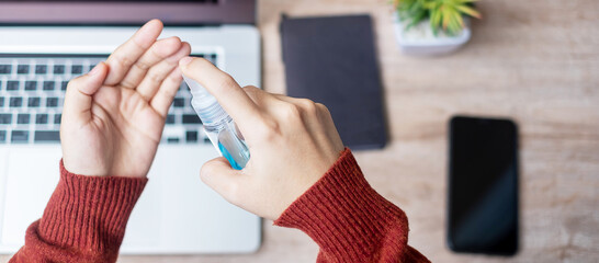 Woman cleaning hands by alcohol sanitizer over laptop and smartphone devices on workplace during work at home, protection coronavirus (Covid-19) infection. Personal hygiene and New Normal concept