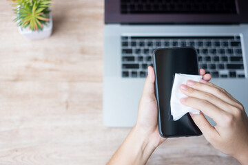 Woman cleaning smartphone and laptop by wet wipes tissue and alcohol disinfectant on workplace during work at home, protection coronavirus (Covid-19) infection. Clean surface and New Normal concept