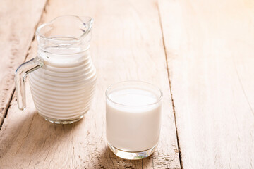 Fresh milk in a glass and in a jug, put on a wooden table