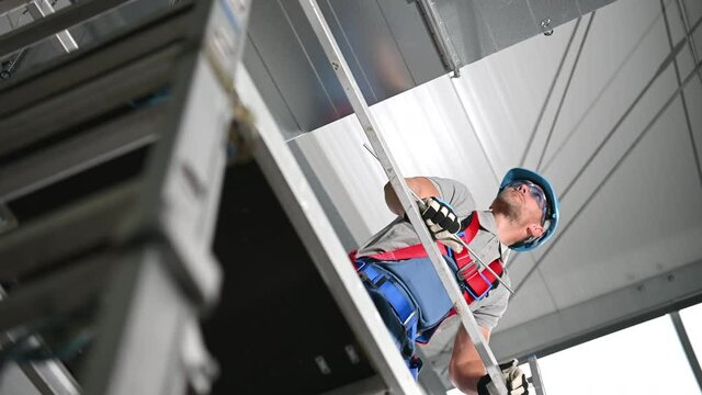 Male Worker Standing On Scaffold And Adjusting Newly Installed Air Conditioner Shaft. Holding Metal Part In Hand And Looking Down. 