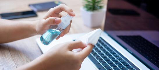 Woman cleaning laptop and smartphone by wet wipes tissue and alcohol disinfectant on workplace during work at home, protection coronavirus (Covid-19) infection. New Normal and Clean surface concept