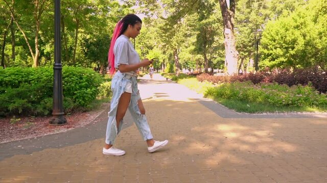 side view african young woman chatting online holding mobile walking on the street slow motion