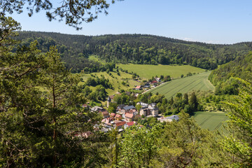 Blick auf Dorf in Thüringen zwischen  bewaldeten Hügeln mit  blauem Himmel