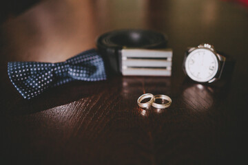 A man's and woman's wedding rings . A man's wrist watch is in the background out of focus.