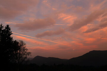 Colori del tramonto in collina con nuvole rosa e scie degli aerei