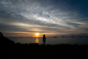 Silhouette of a woman watches sunset over a sea or ocean on a tropical island.