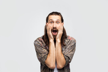 Oh my God! Expressive emotion of surprise and shock, grabbed his face with his hands and opened his mouth and eyes wide. Hipster traveler stylish carefree man on a white studio background