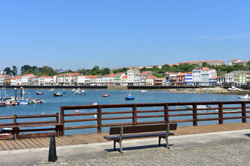 Fototapeta na wymiar Fishing village with wooden boardwalk, bench and boats with blue sky. Mugardos, Galicia, Spain.