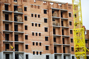 Big yellow construction crane on a background of a brick house. The concept of construction of multi-storey buildings. Heavy construction equipment. Building and crane. High load capacity.