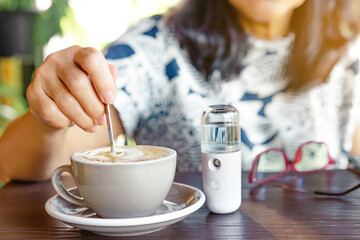 A quarantined woman relax with hot cappuccino coffee and alcohol nano mist sprayer on table while...