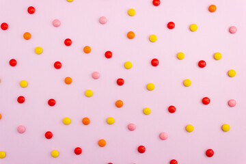 Polka dot pattern made of multicolored chocolate candies on a pink background. Top view, layout.