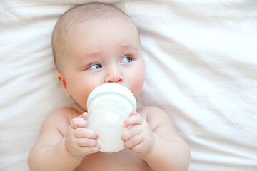 Beautiful baby eating milk from bottle in white bedroom on white background