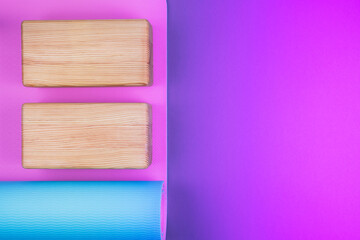 Top view of blue pink yoga mat and two wooden blocks on neon colored pink purple background. Yoga, pilates or sport concept. Flat Lay. Place for text.