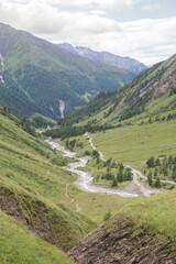 Fototapeta na wymiar Mountain river, tourist route and a green valley between the mountains in Austrian Alps. View from the way to Grossglockner rock summit, Kals am Grossglockner, Austria