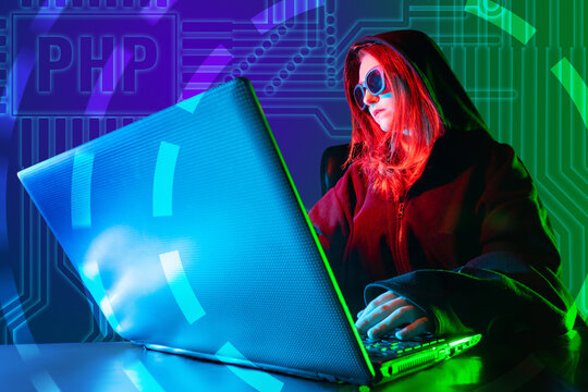 Girl programmer near computer. Programmer writes PHP code. Woman works PHP developer. Freelancer with glasses and hood. Website development. Website development using PHP. Web application developer