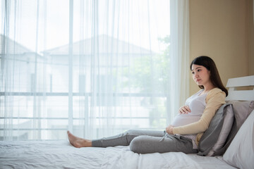 Obraz na płótnie Canvas Mom waiting and expecting baby has good health Happy pregnant young asian woman touching abdomen and admiring baby or fetus on bed with happiness smile face. Asia pregnancy mother love baby so much. 