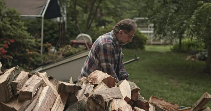 Straight on shot looking over woodpile of man taking freshly split red oak fire woodcut from wheelbarrow to stack - with audio
