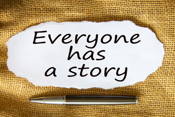 The text 'everyone has a story' on white paper. Metalic pen. Beautiful canvas background. Business concept.