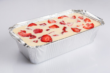 isolated close corner view of a Russian zapekanka strawberry pudding cottage ice cream cheese cake in a foil baking pan on a white background