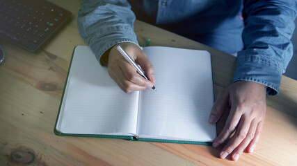 Anonymous man is studing and writes in a notebook on working desk at night. Person writes a letter....