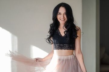 Fototapeta premium beautiful happy girl in a black top and pink skirt against the gray walls near the window