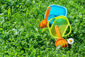 Baby toys a shovel and bucket on green meadow background with copy space.