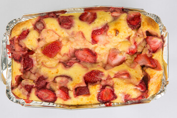 vertical close up flat lay top view of a Russian baked zapekanka strawberry pudding cottage ice cream cheese cake in a foil baking pan on a white background