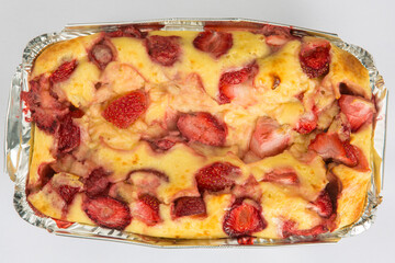 vertical close up flat lay top view of a Russian baked zapekanka strawberry pudding cottage ice cream cheese cake in a foil baking pan on a white background