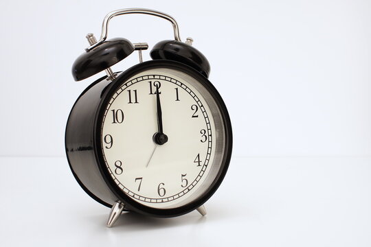 Black vintage alarm clock on table. White background. Wake up concept. An image of a retro clock showing 00:00/12:00 pm/am.   