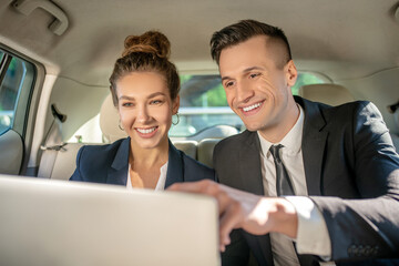 Business man and woman with laptop in back seat in car